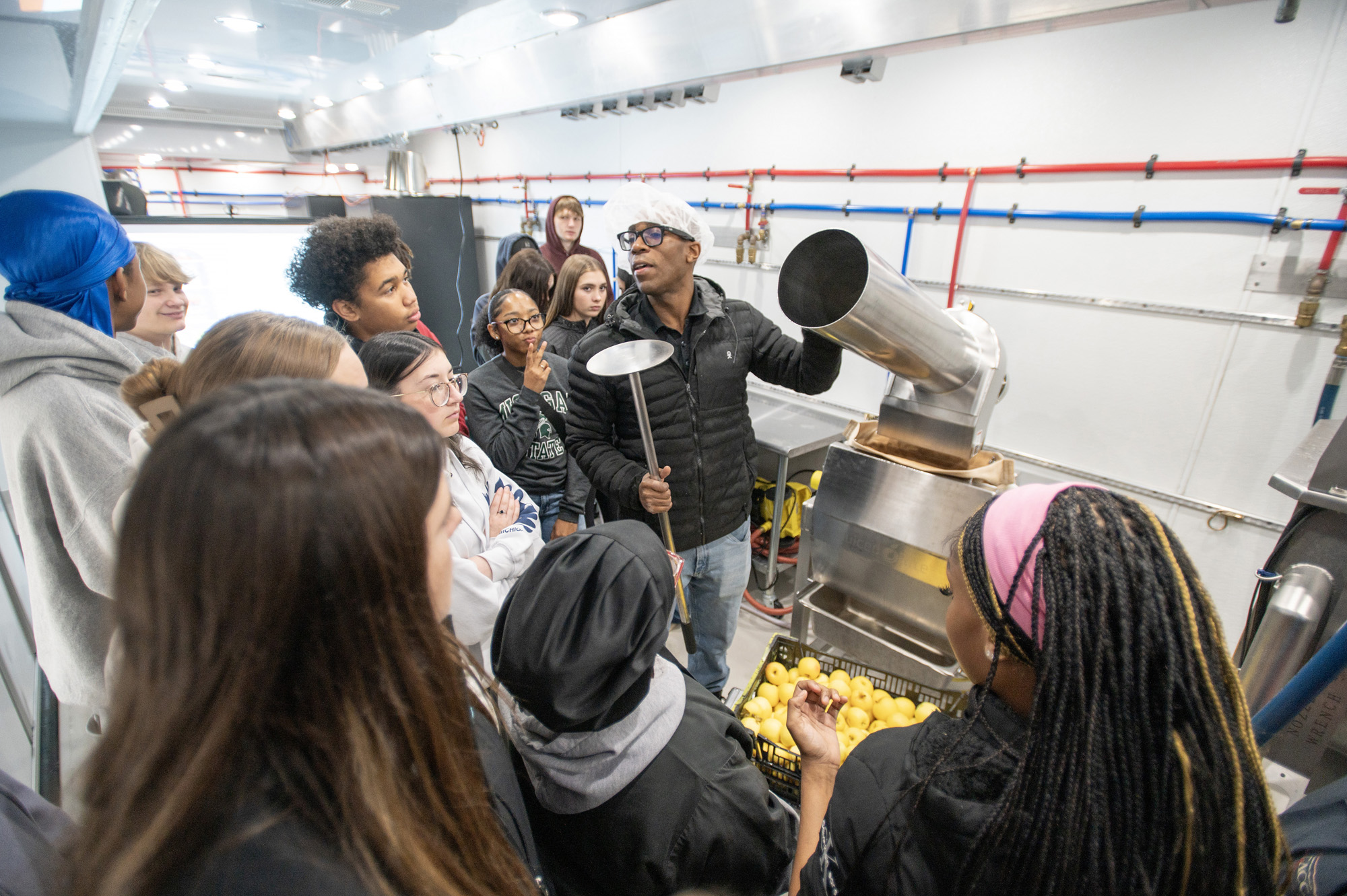 An instructor demonstrates food processing equipment to a group of students inside Michigan State University&rsquo;s mobile food processing lab during a workforce training event.